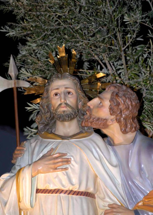 Escultura policromada mostra figura beijando o rosto de outra coroada com auréola dourada, representando o beijo de Judas a Jesus.