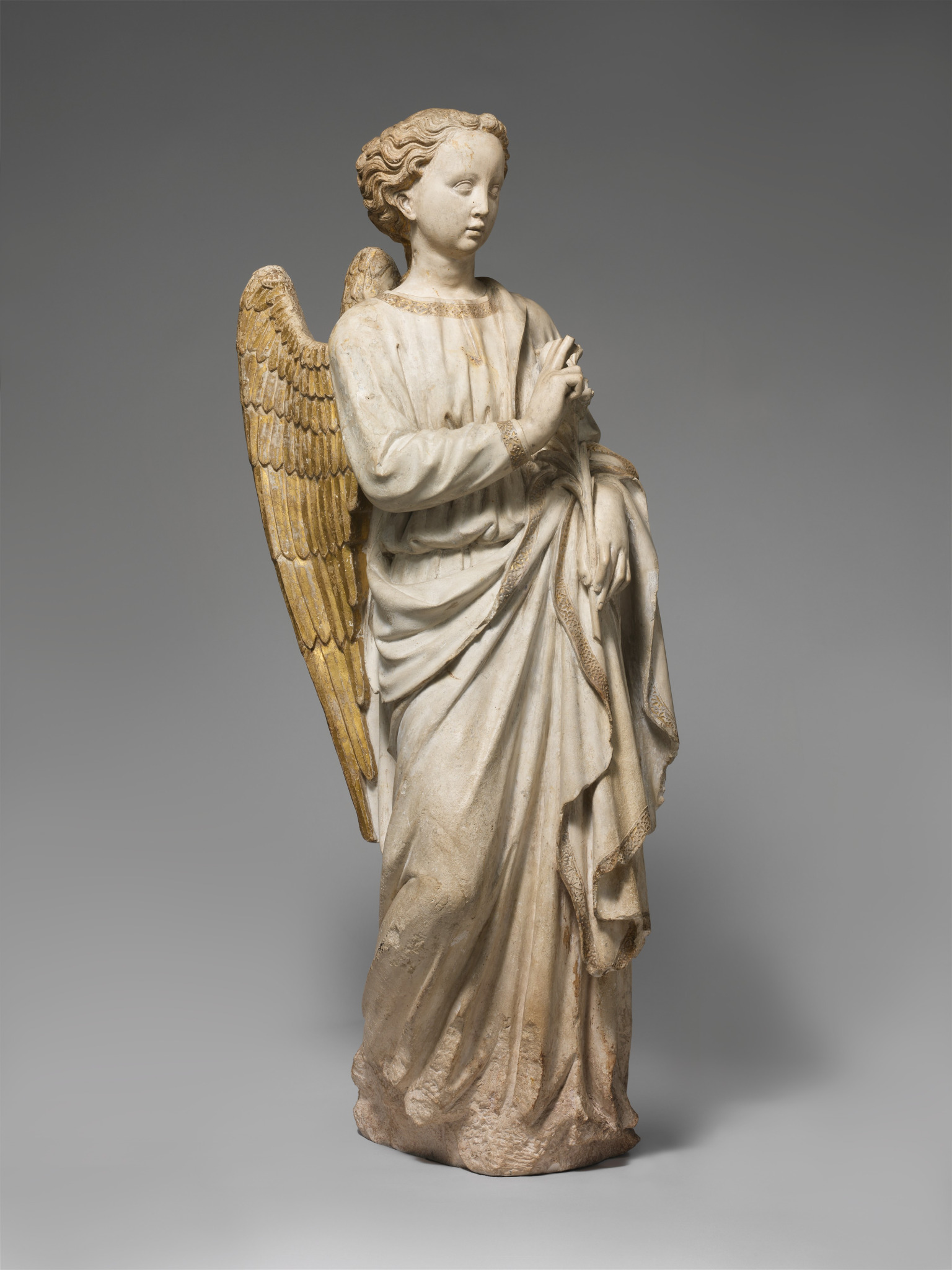 Escultura gótica de anjo em oração, com asas douradas e vestes longas, obra europeia do século XV.